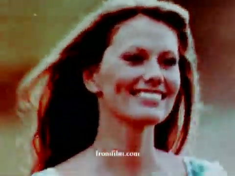 The still features a smiling woman with flowing hair, evoking a joyful and carefree vibe. The colors are warm and vibrant, highlighting a nostalgic feel typical of vintage commercials. The background is blurred, focusing attention on her expression, and it captures the essence of the 1972 Volkswagen 'station wagon' theme. The color correction enhances the image while maintaining its retro charm.