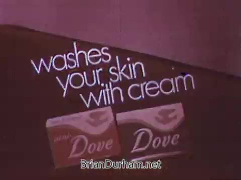 The still from the 1968 Dove Soap commercial features a simple yet effective graphic design. It prominently displays the text 'washes your skin with cream' alongside two packages of Dove soap. The background is likely a soft or muted color, enhancing the focus on the product and its message about moisturizing benefits. The overall aesthetic aligns with the advertising style of that era, aimed at promoting skin care.
