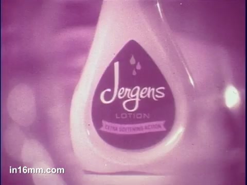 The still features a close-up of a Jergens Lotion bottle, showcasing its distinctive shape and branding. The label prominently displays the “Jergens” name and emphasizes 'Lotion' along with the phrase “Citrus Softening Action.” The color scheme has a soft, pastel-like quality, enhancing the product's appeal. The background appears blurred, drawing focus to the lotion's packaging.