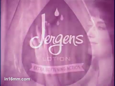 The still features a pink-toned background with the Jergens logo prominently displayed in the center, surrounded by a droplet design. The text highlights 'Jergens Lotion' and 'Extra Softening Action.' In the background, a woman gazes at the camera, enhancing the commercial's focus on beauty and skincare.