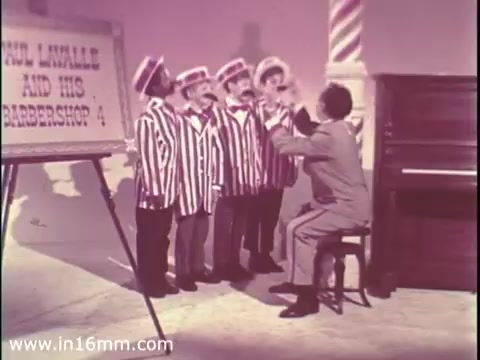 The still features a group of boys in striped blazers standing together, facing an adult seated at a piano. The adult appears to be engaging them in a musical performance or rehearsal. A sign nearby, likely promoting The Boys Club, is visible in the frame. The setting has a colorful, playful atmosphere typical of a 1960s public service announcement.