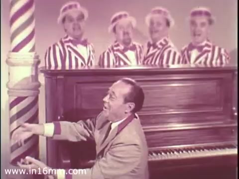 The still shows a performer at a piano with a cheerful expression, engaging with the audience. Behind him, four singers dressed in striped suits and hats appear, adding a lively atmosphere to the scene. The setting has a vintage feel, typical of the 1960s, emphasizing camaraderie and entertainment in the context of a public service announcement for The Boys Club. The colors are vibrant and the composition evokes a sense of joy and community.