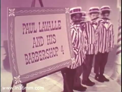 The still features a sign reading 'PAUL LAVALLE AND HIS BARBERSHOP 4' prominently displayed. In front of the sign, a group of four young boys dressed in striped outfits stands in a line, likely representing a barbershop quartet. The overall aesthetic suggests a cheerful and engaging atmosphere, typical of public service announcements from the late 1960s. The colors appear soft, characteristic of the 16mm print format.