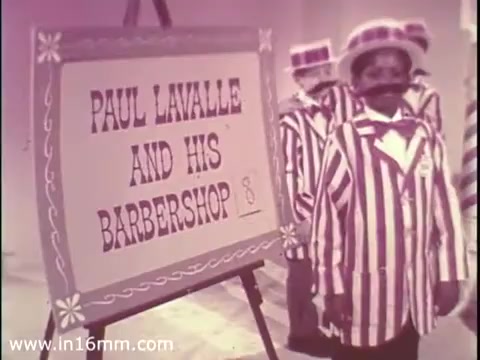 The still depicts a scene from a 1968 public service announcement for The Boys Club, showcasing performers dressed in striped outfits, standing in front of a sign that reads 'PAUL LAVALLE AND HIS BARBERSHOP.' The setting has a playful and vibrant atmosphere, likely aiming to engage a young audience. The visual style is characteristic of the period, with bright colors and a whimsical presentation.