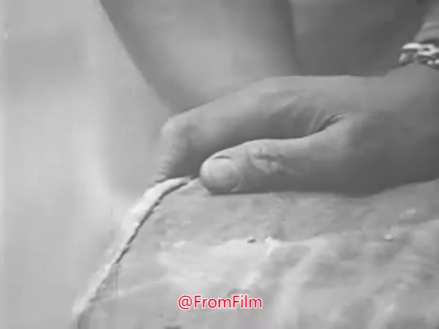 The still from 'Project CARE PSA - 1960's' depicts a close-up of a hand resting on what appears to be a textured surface. The hand is positioned gently, suggesting care or attention. The background is blurred, emphasizing the hand and its connection to the object, which could symbolize themes of support or nurturing. The monochrome film gives it a vintage aesthetic typical of the era.