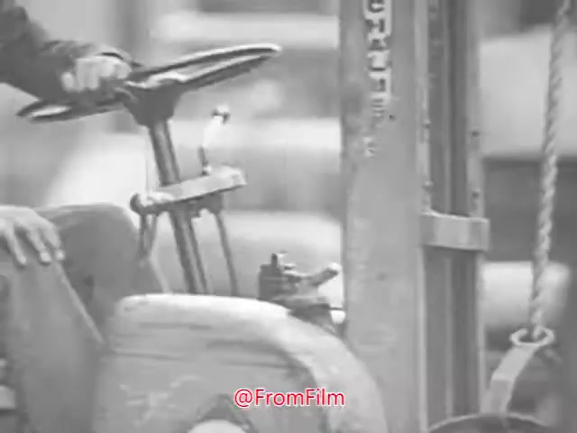 The still from 'Project CARE PSA - 1960's' features a close-up of a person's hands on the steering wheel of a forklift. The focus is on the machinery's controls, emphasizing its industrial context. The black-and-white aesthetic reflects the era, showcasing the equipment used in that period. The scene likely highlights safety or operational practices relevant to the project's theme.