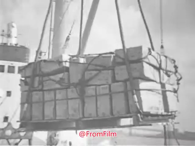 The still from the 1960s 'Project CARE PSA' shows a cargo-laden crate being lifted by a crane, likely on a ship. The scene captures a moment of logistical operation, emphasizing themes of aid or support, typical of public service announcements from that era. The image is in black and white, adding to its historical context.