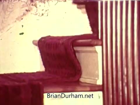 The still from the 'National Safety Council PSA' depicts a close-up of a staircase featuring a carpet runner. The focus is on the texture of the carpet, showing how it is laid over the stairs. The scene emphasizes safety by highlighting the potential hazards of stairs, likely aiming to promote awareness of proper stair use and caution. The colors appear muted, typical of older film stock.