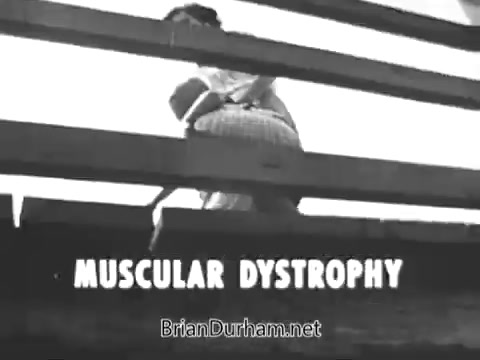 The still from the 'Jerry Lewis Muscular Dystrophy PSA' depicts a laborer, Arnold Hughes, working diligently under the sun, showcasing his physical strength. The scene contrasts his pride in his abilities with the poignant reality of his son, Spunky, who struggles with muscular dystrophy, unable to perform simple physical activities independently. This highlights themes of love, perseverance, and the impact of muscular dystrophy on families.