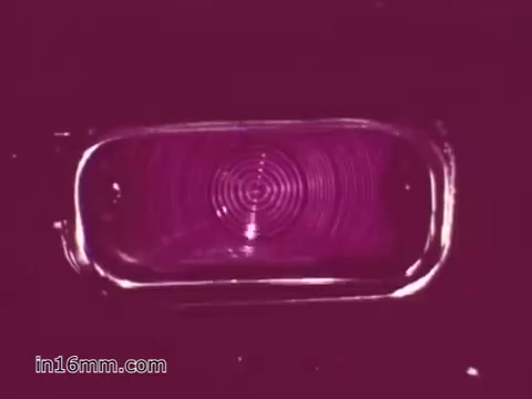 The still from the 'West Virginia Safety Council PSA' features a close-up view of a vehicle's light, possibly a lens or reflector. The image is defined by a vivid purple background, emphasizing the circular patterns and textures of the light component. This visual likely underscores the importance of vehicle safety inspections during the 1960s, promoting awareness of car maintenance and safety features. The film appears to convey a message about ensuring vehicles are in proper working order for the safety of drivers and passengers.