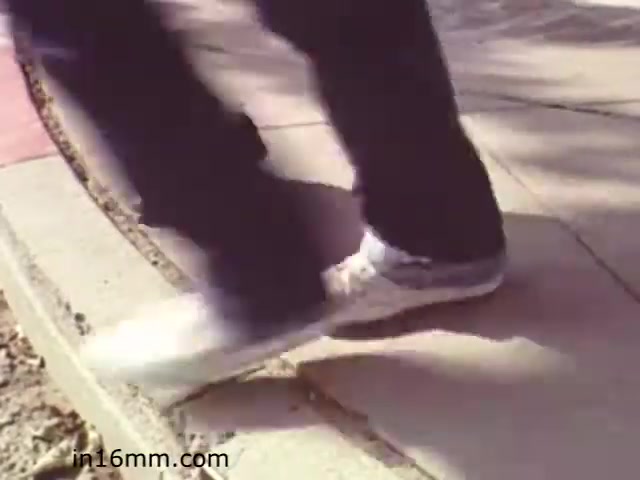 The still from 'Walk Safely' features a close-up of a person's feet walking on a sidewalk. The individual is wearing sneakers, and the focus is on their movement, possibly highlighting pedestrian safety. The film, likely aimed at educating viewers about safe walking practices, captures a moment that emphasizes vigilance while walking, possibly along a curbed path. The overall tone is instructional, reflecting the educational nature of the film from 1982.