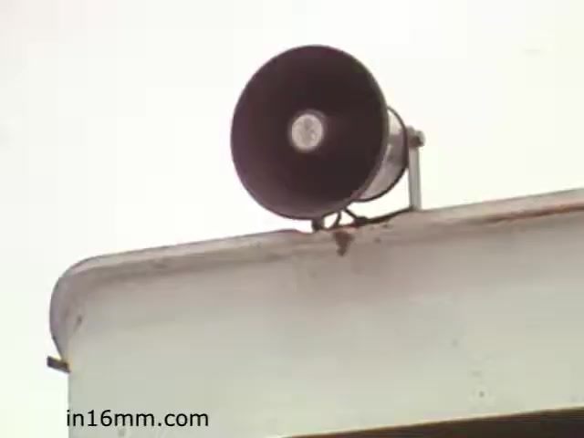 The still from 'Walk Safely,' an educational film from 1982 produced by Fiesta Films, depicts a loudspeaker mounted on a building. The focus is on the speaker, suggesting it may be used for announcements or warnings related to safety. The context likely relates to pedestrian safety education, emphasizing vigilance and awareness in outdoor environments. The film, representative of the era's instructional approach, aims to inform viewers about walking safely, potentially targeting schools or community settings.