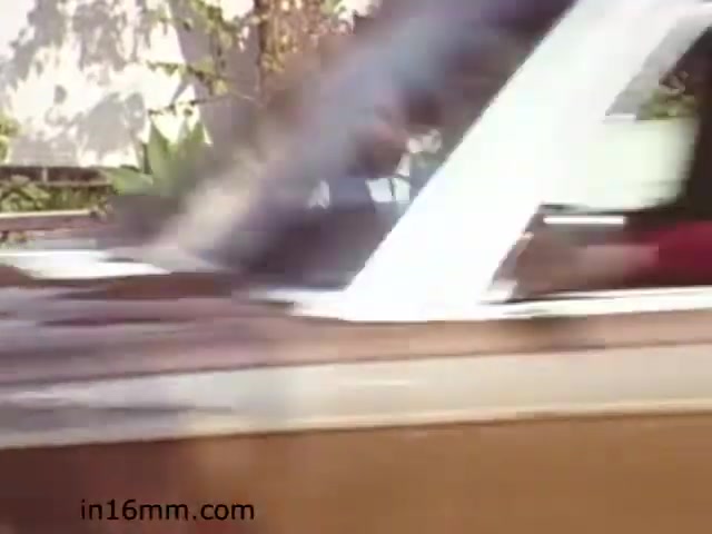 The still from 'Walk Safely,' an educational film from 1982 by Fiesta Films, captures a motion-blurred scene featuring a car in motion. The focus appears to be on promoting pedestrian safety, likely emphasizing the importance of awareness in traffic. The background hints at a suburban setting, with greenery visible, typical of the era’s aesthetic. The film likely aims to instruct viewers on safe walking practices, particularly around vehicular traffic.