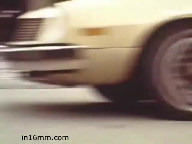 The still from 'Walk Safely,' an educational film from 1982 by Fiesta Films, likely depicts a scene involving a vehicle, emphasizing road safety. The focus appears to be on the movement of a car, which could relate to themes of pedestrian awareness or safe driving practices. The film likely aims to educate viewers on the importance of being mindful around traffic.