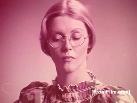 The still from the 1970s 'Life Savers Gum' advertisement showcases a woman with glasses and an intense expression. She's wearing a distinctive floral-patterned dress. The image features a primarily pink color palette, creating a nostalgic feel typical of that era's advertising. The overall aesthetic reflects the playful and vibrant style used in promotional materials of the time.