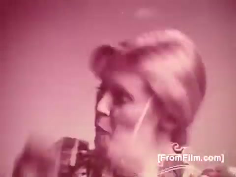 The still from 'Life Savers Gum - 1970's' features a woman with light hair, expressing delight or enjoyment. The color tone appears muted, likely due to the age of the 16mm print, contributing to a nostalgic aesthetic typical of that era. The setting seems simple, focusing on the subject's reaction, likely showcasing the product's appeal.