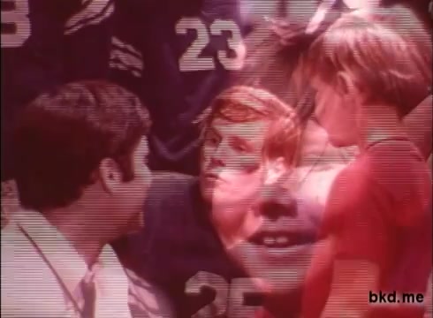 The still from a 1970s Crest toothpaste commercial features a vibrant montage of faces, including a coach and young athletes. The image conveys a sense of teamwork and enthusiasm, highlighted by the contrasting red and blue tones. Numbers, likely representing athletes' jerseys, add a sporty context, while the overall composition reflects the energetic and optimistic style typical of that era’s advertising.