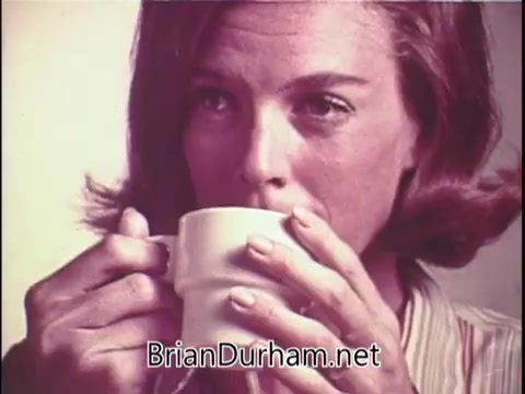 The still features a woman with short, styled hair holding a white coffee cup close to her face as she prepares to take a sip. The focus is on her expression and the cup, evoking a sense of enjoyment or contemplation. The background is softly blurred, emphasizing the subject and the act of drinking coffee, likely in the context of promoting Max-Pax coffee.