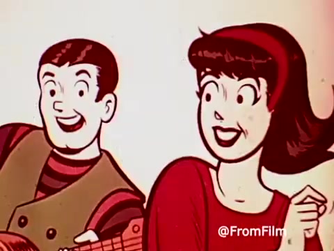 The still features two animated characters, a boy and a girl, both with cheerful expressions. The boy, holding a guitar, seems to be singing or playing music, while the girl looks delighted, possibly encouraging him. The vibrant colors and cartoonish style reflect the playful and upbeat nature typical of 1960s commercials, promoting Archies Alpha Bits cereal along with the associated merchandise.