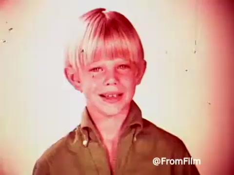 The still features a young boy with a bright blonde bowl cut, smiling directly at the camera. He is wearing a green shirt, and the background appears to be softly lit, giving a nostalgic, warm tone typical of 1960s advertising. This frame likely promotes Archie's car, connecting it to Post Alpha Bits cereal in a playful manner aimed at children.