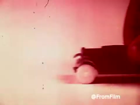 The still from the 'Archies Alpha Bits' commercial features a vibrant, stylized depiction of Archie's car from the 1960s. The image is saturated with a pink hue, enhancing the nostalgic feel. The close-up shows the car's wheel in motion, conveying a sense of fun and excitement associated with the cereal promotion. The overall aesthetic reflects the playful and colorful design typical of that era's advertising.