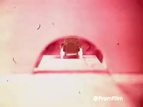 The still from the 'Archies Alpha Bits' commercial features Archie's car moving through a vibrant, colorful tunnel. The image is marked by a retro aesthetic typical of the 1960s, with a focus on the car's playful design. The background appears blurred, enhancing the sense of motion and excitement associated with the cereal promotion. The overall atmosphere is whimsical, appealing to a youthful audience.