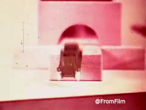 The still from the 1960s Archies Alpha Bits commercial features a toy car prominently placed on a simple set. The scene is likely meant to promote the car as part of a playful, cereal-themed marketing strategy. The image has a warm tone, characteristic of 16mm film, with a slightly dreamy quality that evokes nostalgia for classic childhood products.