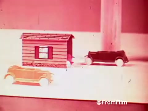The still features a colorful scene from the 1960s Archies Alpha Bits commercial, showcasing toy cars—one orange and one black—driving near a small, exaggerated model house. The visual style is vibrant and playful, characteristic of children's advertising from that era, emphasizing fun and imagination. The overall aesthetic has a retro quality typical of 16mm prints, likely aimed at promoting both the cereal and the associated toy as engaging elements for kids.