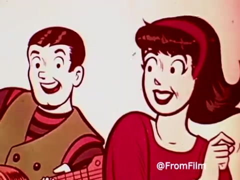 The still features characters from the 1960s Archies Alpha Bits commercial, showcasing a cheerful scene. One character holds a guitar while another, smiling broadly, engages with the viewer. The colorful, cartoonish style emphasizes a fun and lively atmosphere, promoting the cereal in an enjoyable manner. The overall vibe captures the playful essence of the era.