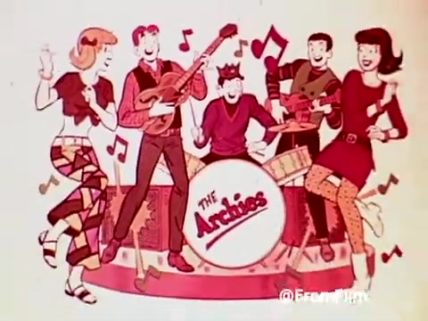 The still features animated characters from 'The Archies', showcasing a musical performance. The group includes a blonde girl and characters dressed in colorful outfits, playing instruments and singing. Musical notes surround them, emphasizing the upbeat vibe. The band is centered around a large drum displaying the band's name, 'The Archies,' promoting the fun and playful spirit associated with Post Alpha Bits cereal in a 1960s context.
