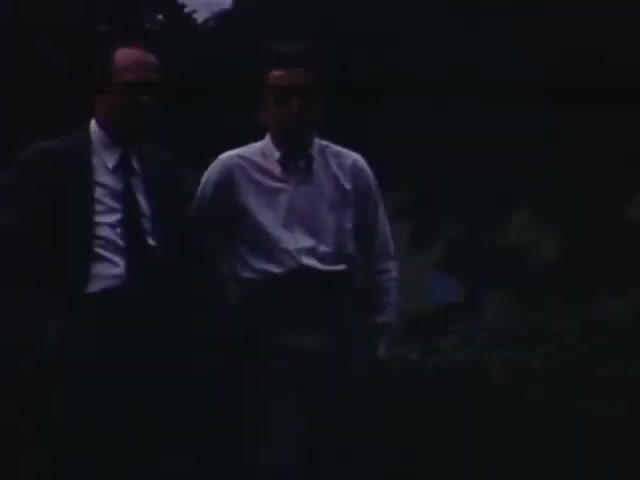 The still from 'Jack #2' features two men walking closely together, likely engaged in conversation. The image, captured on Kodachrome film from 1941-1943, suggests a candid moment with soft lighting and a natural outdoor setting. The men are dressed in semi-formal attire, indicative of the era's style, with one in a suit and the other in a buttoned shirt. The background is slightly blurred, focusing the viewer's attention on their interaction.