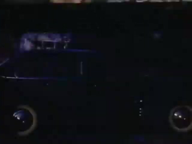 The still depicts a vintage vehicle, likely from the early 1940s, shown in low light. The ambiance is moody, highlighting the silhouette of the car with subtle reflections. Its rounded features and classic wheels suggest a time before modern design, capturing a nostalgic moment typical of Kodachrome film from that era. The overall feel evokes a sense of mystery or nostalgia, reflective of the years 1941-1943.