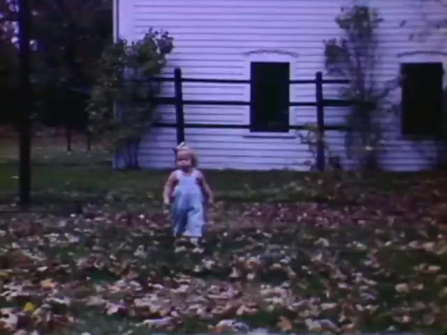The still from 'Connie & Patty #2' features a young child wearing overalls, walking through a yard scattered with fallen leaves. In the background, there is a white house with pointed windows, typical of mid-20th century architecture. The film’s aesthetic and the child’s clothing suggest it may be from the 1940s, aligning with your guess of a WW2 timeframe, particularly as it utilizes Ansco film, which was less common than Kodak during that period.