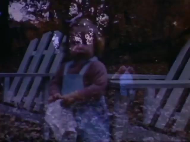 The still features a child in a casual outfit, possibly from the mid-20th century, amidst a backdrop of autumn foliage and a white wooden fence. The use of Ansco film suggests a date likely in the early to mid-1940s, aligning with your guess of the WW2 timeframe. The composition hints at a nostalgic or familial theme typical of home movies from that era. The soft focus and color palette evoke a vintage feel, characteristic of films from that period.
