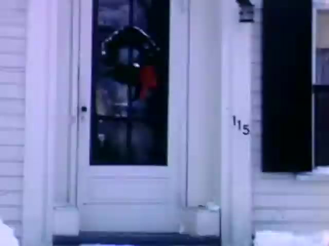 The still from 'Connie & Patty #2' shows a snowy scene focused on a white house with a front door adorned with a Christmas wreath. The presence of snow indicates winter, and the style of the house may suggest a mid-20th century American aesthetic. Given the context and the film stock (Ansco), your guess of a World War II timeframe seems plausible, likely placing it in the 1940s.