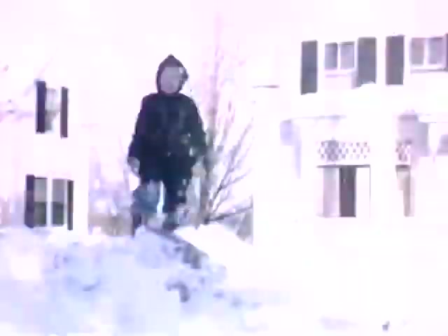 The still from 'Connie & Patty #2' features a child in winter clothing, standing on a snowbank, suggesting a playful winter scene. The setting includes a house with distinctive architecture that may point to a mid-20th century American suburban style. The film's use of Ansco film stock rather than Kodak may imply a release period likely around the 1940s, potentially during or shortly after WWII. The overall aesthetic evokes nostalgia, common in home movies of that era.