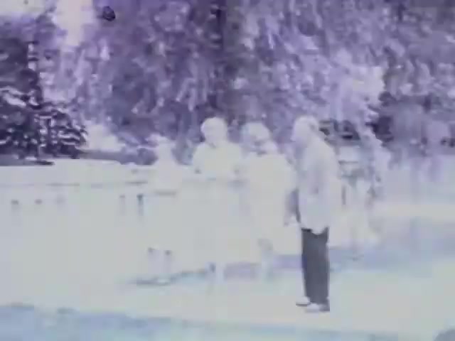 The still from 'Pat in Ocean - 1955' features a group of four individuals standing near a wooden fence, surrounded by trees. The image is in black and white, exhibiting a soft focus and light exposure, giving it a nostalgic, vintage feel. The people appear to be engaged in conversation, with one man in a suit and the others in lighter attire, suggesting a casual gathering or outing.
