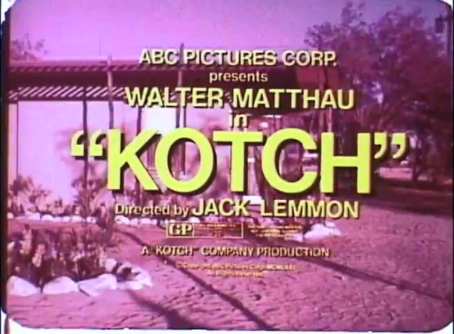 The still features vibrant, colorful text announcing the film 'Kotch,' starring Walter Matthau and directed by Jack Lemmon. The title is prominently displayed in yellow against a backdrop that suggests an outdoor setting, possibly a garden or park. The overall aesthetic is reminiscent of vintage promotional materials, emphasizing a lighthearted and nostalgic tone. The print quality reflects typical characteristics of a 16mm format, with slightly soft edges and a warm color palette.