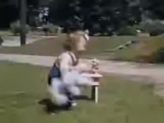 The still features a young child playing outdoors, seated at a small table on a grassy area. The vibrant colors typical of Kodachrome film from 1941 enhance the nostalgic ambiance. The setting appears to be a park or garden, likely emphasizing a carefree moment in childhood.