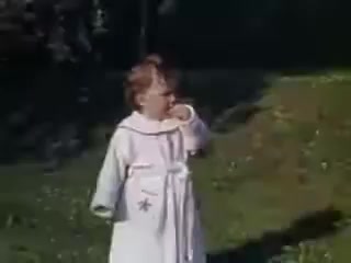 The still features a young girl wearing a light-colored coat with a star design, standing outdoors in a grassy area. She appears to be gazing off to the side, possibly engaged in thought or observation. The scene's colors suggest vibrant summer lighting typical of the Kodachrome film from 1941, capturing a nostalgic moment from childhood.
