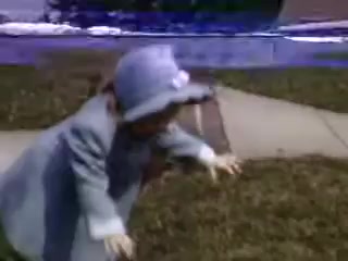 The still from 'Connie and Shirley reel #1 - 1941' features a child in a light blue outfit and hat, seemingly in a playful position on a grassy surface. The background includes a sidewalk, hinting at an outdoor setting. The Kodachrome color palette reflects the vibrant hues typical of vintage film from that era.