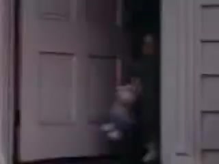 The still depicts a young child standing in a doorway, appearing to playfully emerge with a stuffed animal. The setting suggests a home entrance, characterized by a light-colored door and surrounding structure typical of the early 1940s. The image captures a moment of youthful innocence and nostalgia, reflective of the era's family dynamics and childhood play.