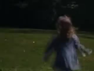 The still from 'Connie and Shirley reel #1 - 1941' depicts a young girl with long hair running through a grassy field. The image captures a moment of playful movement, likely during a sunny day, with a soft focus enhancing the nostalgic feel of the Kodachrome film from 1941. The background is blurred, emphasizing the child's joyful activity.