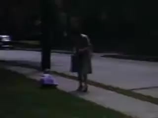 The still from 'Connie and Shirley reel #1 - 1941' depicts a young girl standing on a sidewalk, possibly examining something on the ground. She wears a dress and appears to be in a suburban setting, with a tree nearby and a street visible in the background. The colors suggest it was shot on Kodachrome film, capturing the essence of early 1940s everyday life.