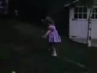 The still features a young girl wearing a striped pink dress, playing outdoors. She appears to be in motion, possibly running or skipping, with a backdrop of grass and a white shed. The scene is captured in a nostalgic Kodachrome style typical of the early 1940s, conveying a sense of childhood innocence and outdoor exploration.