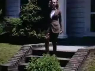 The still from 'Connie and Shirley reel #1 - 1941' features a young woman standing on brick steps in front of a house, likely dressed in fashionable attire of the era. The scene is bright and vivid, typical of Kodachrome's color depth, with lush greenery surrounding the steps. The setting conveys a sense of mid-20th century suburban life.
