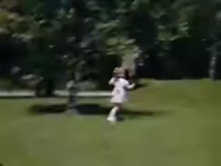 The still from 'Connie and Shirley reel #1 - 1941' showcases a young child running playfully across a vibrant green lawn. The scene captures a sense of joy and freedom, highlighted by the bright colors typical of Kodachrome film from that era. Trees are visible in the background, suggesting a suburban setting. The overall tone invokes nostalgia for childhood and simpler times.