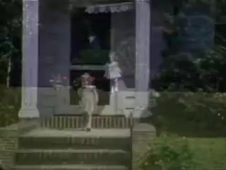 The still from 'Connie and Shirley reel #1 - 1941' features a nostalgic scene captured in Kodachrome. Two children are on the steps of a porch, with one standing and the other seated. The setting is outdoors, likely in a suburban or rural area, characterized by greenery and a homey atmosphere. The colors are vibrant, typical of Kodachrome film, highlighting the innocence and simplicity of childhood in that era. The timestamp places the scene in the early 1940s, evoking a sense of nostalgia.