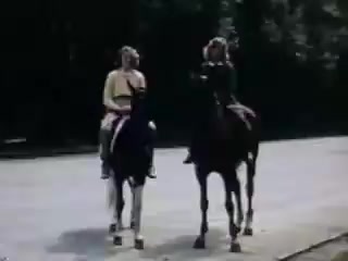 The still features two young women riding horses along a road. The scene is bright and colorful, typical of Kodachrome film from the early 1940s. The women appear to be enjoying their ride, illustrating a leisurely, carefree moment from that era. The background suggests a natural setting, possibly hinting at outdoor activities or adventures.