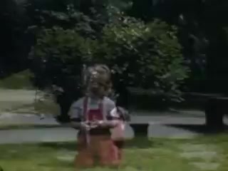 The still features two young girls playing outdoors, dressed in colorful clothing typical of the early 1940s. One girl is prominently positioned in the foreground, holding an object, while the other is slightly behind. The background includes lush greenery and a hint of a park setting, evoking a sense of innocence and childhood playfulness. The vibrant colors suggest the use of Kodachrome film, capturing the moment with a nostalgic feel from 1941.